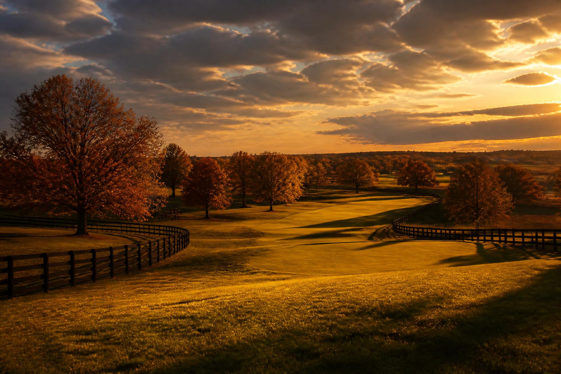 A wide Kentucky fairway at golden hour with board fences and autumn trees